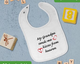 May include: White baby bib with the text "My Grandpa sends me kisses from heaven" in black with two red hearts. The bib is on a light blue background with wooden blocks spelling out "GIRL" and "BOY" and a wooden dragonfly.