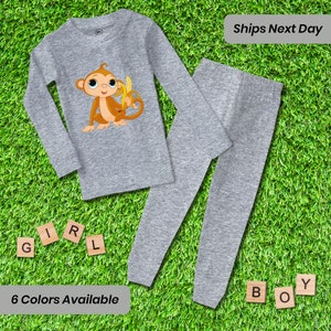 May include: Gray long-sleeved shirt and matching pants with a cartoon monkey holding a banana. The shirt has a monkey graphic and the pants are plain.  6 Colors Available.