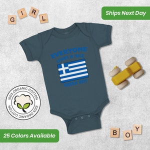 May include: A blue baby onesie with a white Greek flag and the text "Everyone loves a nice Greek boy". The onesie is made of 100% organic cotton.