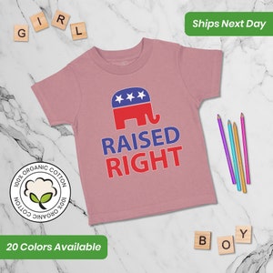 May include: Pink short-sleeved t-shirt with a red, white, and blue elephant graphic and the text "RAISED RIGHT". The shirt is made of 100% organic cotton.