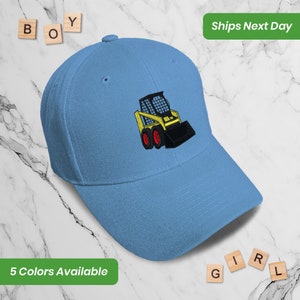 May include: A light blue baseball cap with an embroidered image of a yellow and black skid steer loader. The cap has a curved brim and a structured crown.