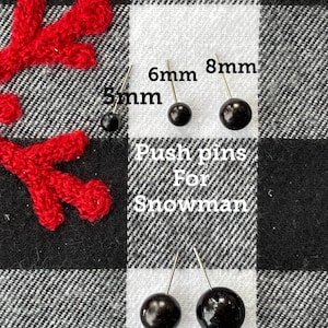 May include: Black push pins in various sizes, 5mm, 6mm, 8mm, 10mm, and 12mm, on a black and white checkered fabric. The text "Push pins for Snowman" is written below the pins.