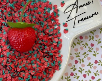 May include: A white ceramic dish filled with red and green strawberry sprinkles. The dish is on a white background with a floral pattern. The text "Annie's Treasures" is written on the dish.