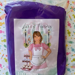 May include: A purple bag with a label that says "Arpi's Treasures" and a cartoon illustration of a woman wearing a pink dress and apron. The bag contains 100 grams of purple modeling clay.