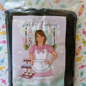 May include: A black bag with a white label that says "Annie's Treasures" and features a cartoon illustration of a woman wearing a pink apron and holding a tray of cupcakes. The label also says "100 grams".