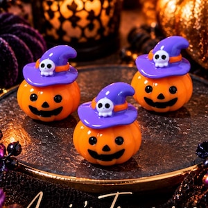 May include: Three small orange jack-o'-lantern figurines, each wearing a purple witch hat adorned with a tiny white skull. The pumpkins feature black painted eyes and mouths. The text "Annie's Treasures" is written in a cursive script at the bottom.