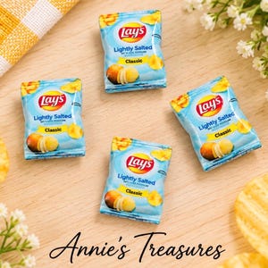 May include: Four miniature Lay's Lightly Salted Classic potato chip bags with blue and yellow packaging, featuring the red Lay's logo, potato chip graphics, and the text Lightly Salted 50% Less Sodium Classic, arranged on a light wooden surface.