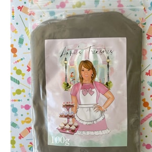 May include: A bag of gray polymer clay with a label that says "Annie's Treasures" and "100g". The label features a cartoon illustration of a woman wearing a pink and white apron and holding a cupcake.