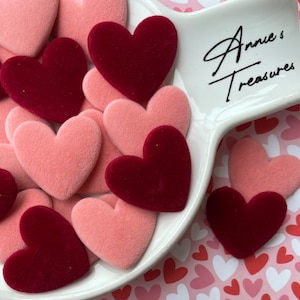 May include: A white ceramic dish with the text "Annie's Treasures" on it, filled with pink and burgundy velvet heart-shaped embellishments.