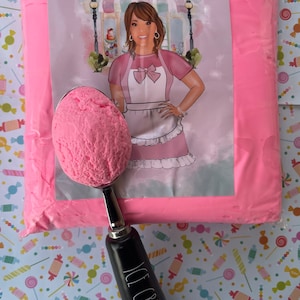 May include: A pink bag of ice cream mix with a scoop of pink ice cream on top. The bag has a label that says "Annie's Treasures". The scoop has a black handle with the words "Ice Cream" written on it.