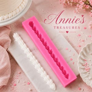 May include: A pink silicone mold with a leaf design, next to a white icing decoration. The image also shows a cake with white frosting and the text "Annie's Treasures". Sprinkles and pink flowers are scattered around the scene.