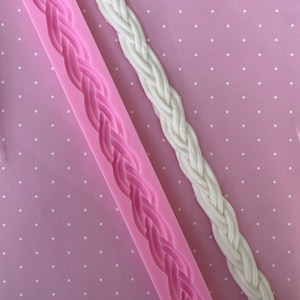May include: A pink silicone mold with a raised design of a braided rope. A white fondant rope is next to the mold.