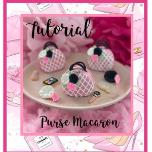 May include: A tutorial on how to make purse-shaped macarons. The image shows three pink macarons decorated with black handles, white flowers, and a pink and white checkered pattern. The macarons are on a pink plate with other decorative elements, including a makeup palette, a small mirror, and a makeup brush.