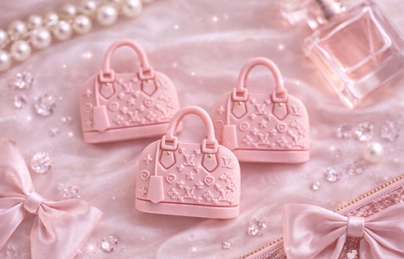 May include: Three light pink, dome-shaped handbags with handles and embossed floral patterns are arranged on a soft, pink surface. The scene includes a pearl necklace, diamonds, and a perfume bottle, creating a luxurious aesthetic.