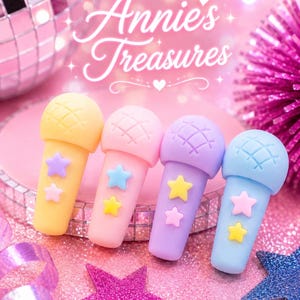 May include: Four pastel-colored microphone-shaped erasers with star accents. The erasers are yellow, pink, purple, and blue, arranged on a pink glitter surface. The text "Annie's Treasures" is displayed in a cursive font.