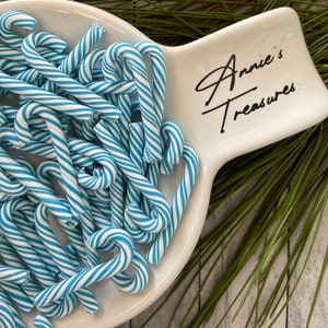 May include: A white ceramic serving dish with the text "Annie's Treasures" in black script. The dish is filled with blue and white striped candy canes.