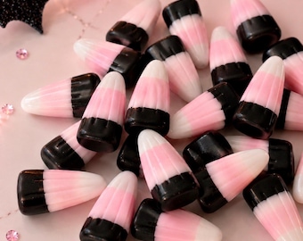 May include: A collection of candy corn pieces featuring a tri-color design of black, pink, and white segments. The text Annie's Treasures is printed at the bottom of the image, which also includes a black glittery bat shape and small pink gems.