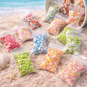 May include: A beach scene with a blue and white polka-dotted bucket spilling colorful sprinkles onto the sand. Several clear bags filled with various sprinkle shapes and colors are scattered around, with a seashell and starfish nearby. The text "Annie's Treasures" is visible.