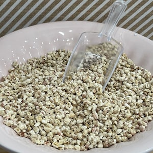 May include: A pink ceramic bowl filled with dried corn kernels. A clear plastic scoop is partially submerged in the bowl.