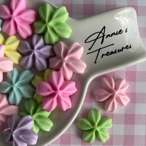 May include: A white ceramic serving dish with a pink and white checkered background. The dish is decorated with the text "Annie's Treasures". The dish is filled with pastel-colored flower-shaped candies.