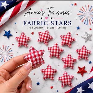May include: Fabric stars in red gingham, 1 inch size, stitched. The image shows several stars, some scattered and one held by a hand. The background includes a marble surface and patriotic decorations, including a flag.