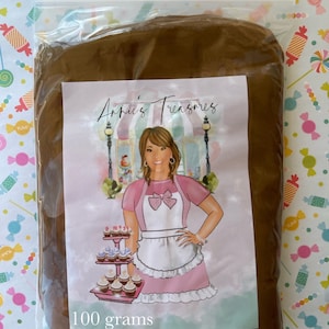 May include: A clear plastic bag containing a mass of brown material. A label features a woman in a pink apron and the text "Arnie's Treasures". The label also states "100 grams". The background is a colorful candy-themed pattern.