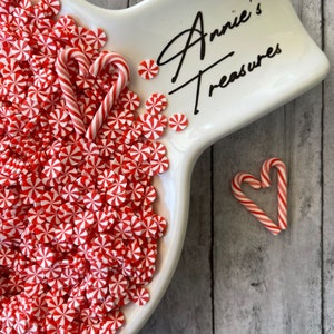 May include: A white ceramic dish with red and white peppermint swirl sprinkles and two red and white candy canes. The dish has the text "Annie's Treasures" written on it.