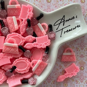 May include: A white ceramic dish with pink and white resin charms in the shape of purses, combs, and perfume bottles. The dish has the text "Annie's Treasures" written on it.