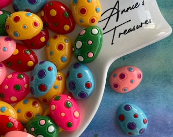May include: A white ceramic dish filled with colorful Easter egg-shaped ornaments. The ornaments are decorated with polka dots in various colors, including red, yellow, blue, green, and pink. The dish has the text "Annie's Treasures" written on it.