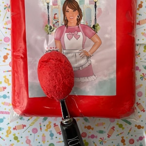 May include: A red fondant icing in a clear plastic bag with a black ice cream scoop. The bag has a label that says "Annie's Treasures" and features a cartoon illustration of a woman wearing a pink and white dress.