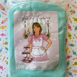 May include: A clear plastic bag containing a mass of light blue material. The bag has a label with the text "Annie's Treasures" and an illustration of a woman in a pink dress and apron. The label also states "100 grams".