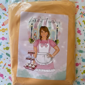 May include: A sealed plastic bag containing a light orange substance. The bag has a label with the text "Annie's Treasures" and an illustration of a woman in a pink dress and apron holding a tray of cupcakes.