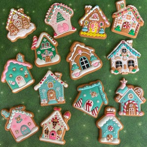 May include: A collection of gingerbread house cookies with colorful icing and decorative details. The cookies feature various designs, including trees, windows, and doors, with pink, blue, green, and white icing. The cookies are arranged on a green surface.