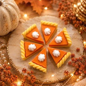 May include: Six triangular slices of orange pumpkin pie arranged in a circle on a round stone plate. Each slice features a pale yellow twisted crust edge and a dollop of white whipped cream on top. The text Annie's Treasures is at the bottom.