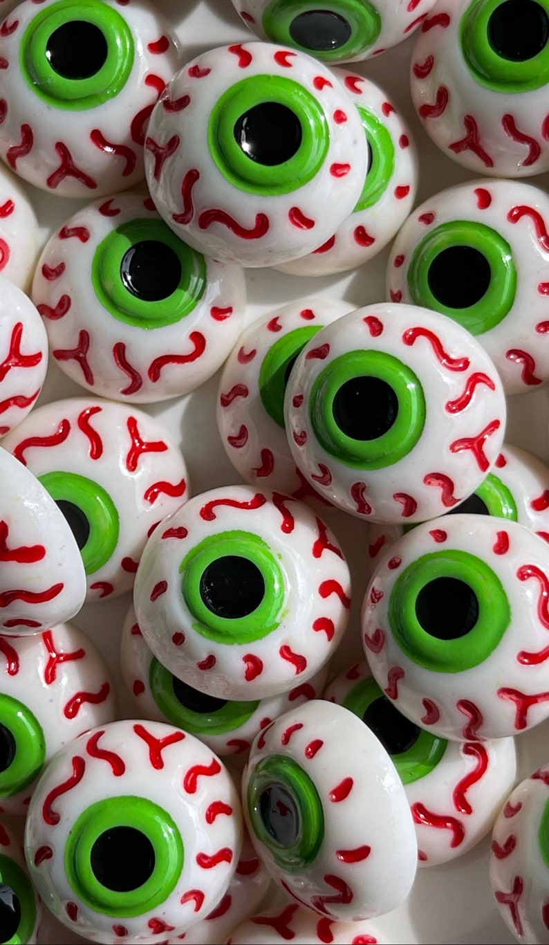 May include: A close-up of several white eyeball-shaped decorations with green pupils and red veins. The decorations are made of a smooth, glossy material and have a realistic appearance.