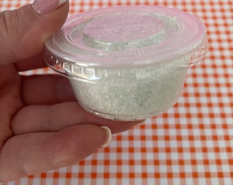 May include: A clear plastic container filled with white sugar crystals. The container has a lid.