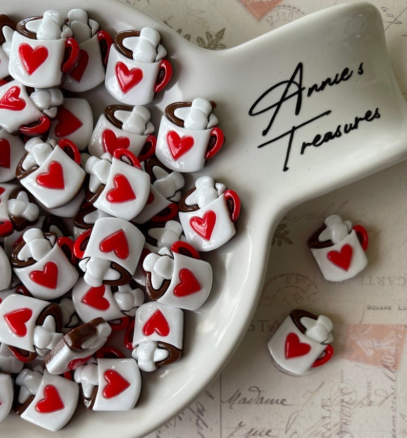 May include: A white ceramic bowl filled with small, white ceramic mugs with red hearts and brown tops. The mugs are arranged in a random pattern. The bowl is on a white surface with the text "Annie's Treasures" written in black.