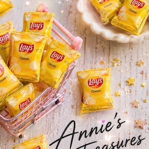 May include: Miniature Lay's Classic potato chip bags in a pink shopping cart and on a white plate. The bags are yellow with the Lay's logo and the word "Classic". The text "Annie's Treasures" is written in cursive.