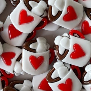 May include: A collection of white ceramic mugs with brown rims and red hearts. Each mug has a white swirl design on the top, resembling whipped cream.