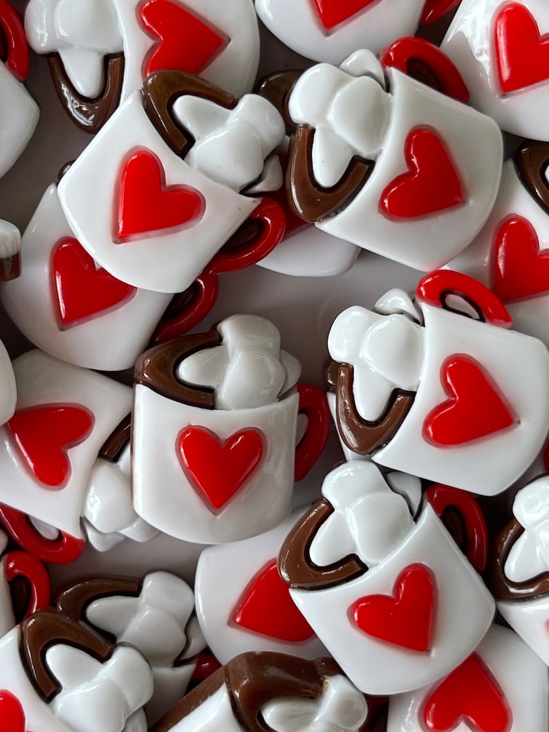 May include: A collection of white ceramic mugs with brown rims and red hearts. Each mug has a white swirl design on the top, resembling whipped cream.
