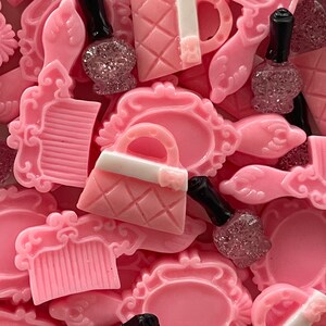May include: A collection of pink resin charms featuring various beauty-themed designs, including a purse, a comb, and a bottle of nail polish. The charms are perfect for adding a touch of femininity to jewelry, crafts, and other projects.