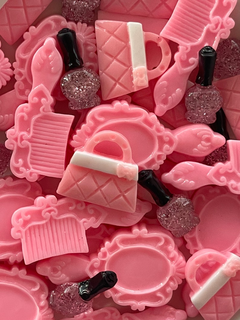 May include: A collection of pink resin charms featuring various beauty-themed designs, including a purse, a comb, and a bottle of nail polish. The charms are perfect for adding a touch of femininity to jewelry, crafts, and other projects.