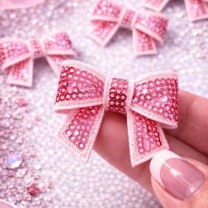 May include: Pink sequined bows with a light pink trim and a glittery background. The bows are held in a hand. The text "Annie's Treasures" is at the bottom of the image.