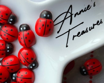 May include: A white ceramic dish with red and black ladybug figurines. The dish has the text "Annie's Treasures" written on it. The dish is on a white background with red hearts and polka dots.