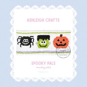 May include: A white smocking plate featuring the text ASHLEIGH CRAFTS and SPOOKY PALS. The design includes three embroidered figures: a black spider, a green Frankenstein monster, and an orange pumpkin, all bordered by green and purple stitching.
