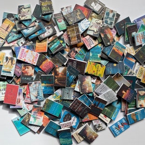Puede incluir: Una gran colecci&oacute;n de libros de bolsillo en miniatura con varios t&iacute;tulos y autores. Los libros est&aacute;n dispuestos en una pila aleatoria sobre una superficie blanca.