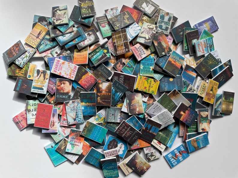 Puede incluir: Una gran colecci&oacute;n de libros de bolsillo en miniatura con varios t&iacute;tulos y autores. Los libros est&aacute;n dispuestos en una pila aleatoria sobre una superficie blanca.