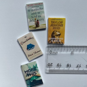 Puede incluir: Cuatro libros de bolsillo en miniatura con diferentes t&iacute;tulos y autores. Los libros est&aacute;n dispuestos sobre una superficie blanca con una regla para la escala. Los t&iacute;tulos son "My grandmother asked me to tell you she's sorry", "The Cheerleaders", "More than this", y "Carrie Soto is back".