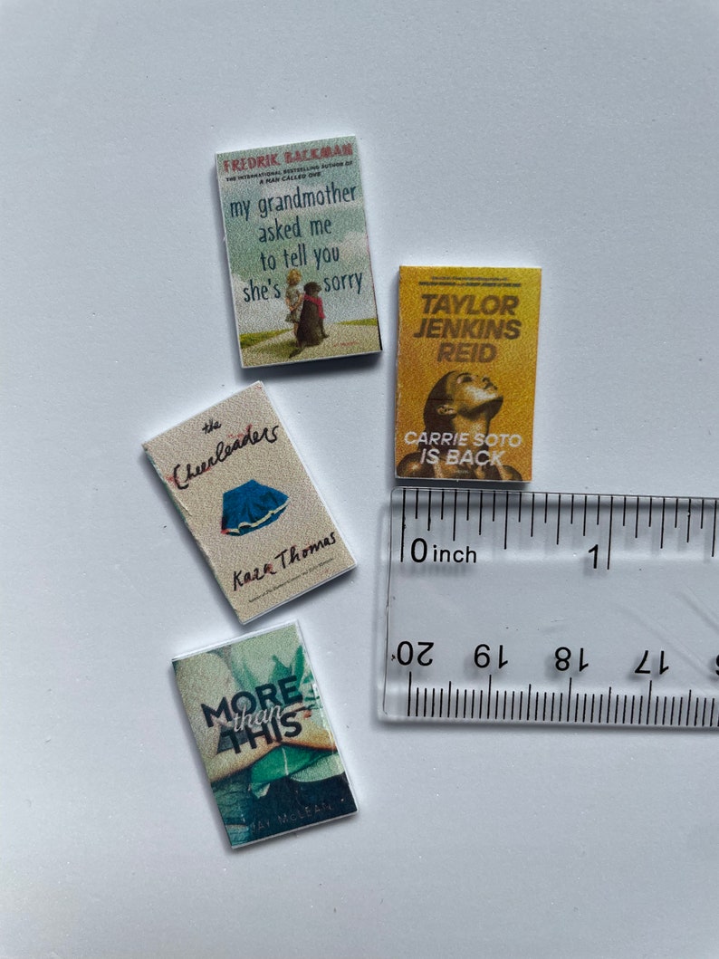 Puede incluir: Cuatro libros de bolsillo en miniatura con diferentes t&iacute;tulos y autores. Los libros est&aacute;n dispuestos sobre una superficie blanca con una regla para la escala. Los t&iacute;tulos son "My grandmother asked me to tell you she's sorry", "The Cheerleaders", "More than this", y "Carrie Soto is back".