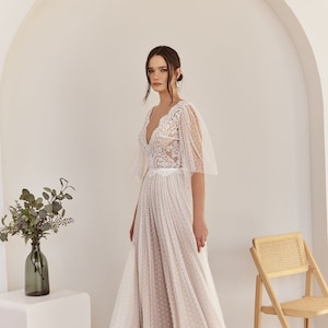 An ivory wedding dress with a lace bodice and a tulle skirt with polka dots. The dress has a V-neckline and short sleeves.